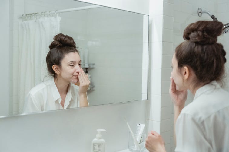 自宅の洗面台でスキンケアをしている女性。丁寧に化粧水を塗っている日常のワンシーン